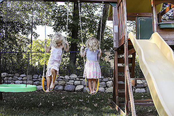 Schwestern stehen auf Schaukeln auf dem Spielplatz