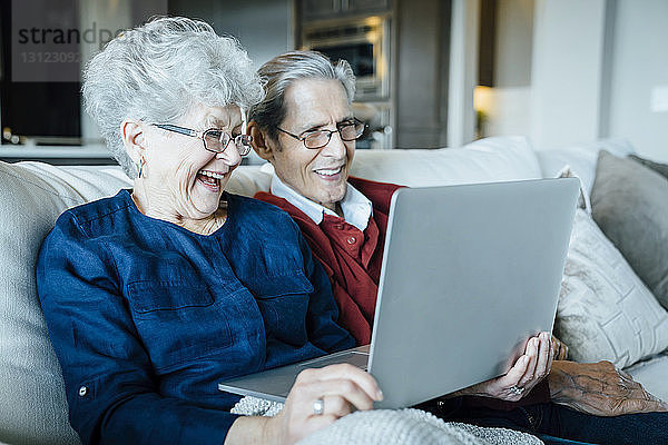 Glückliches älteres Ehepaar bei Videokonferenzen auf dem Sofa sitzend per Laptop