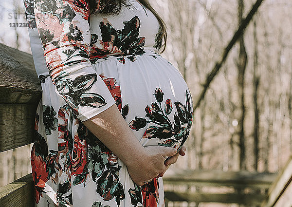 Mittelsektion einer schwangeren Frau  die ihren Bauch berührt  während sie im Wald steht