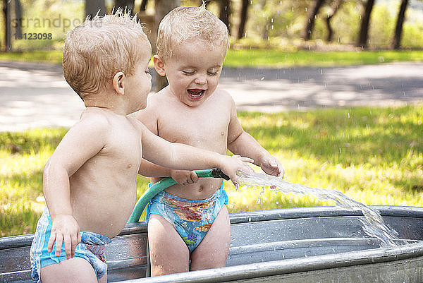 Fröhliche Zwillingsbabys spielen mit Wasser in der Waschwanne