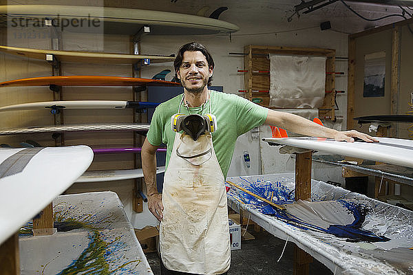 Porträt eines lächelnden Mannes  der im Workshop an Surfbrettern steht