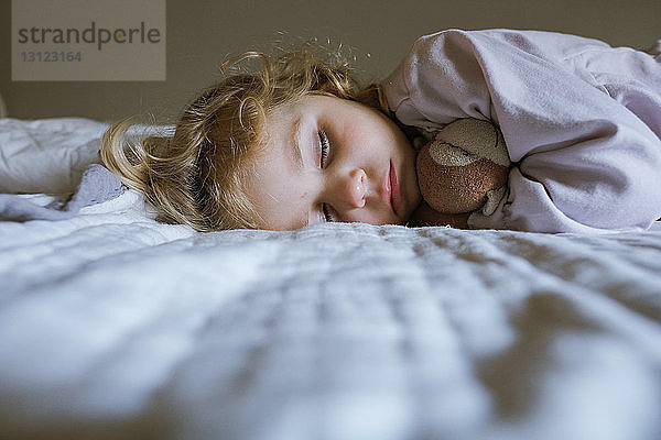 Süßes Mädchen mit Spielzeug  das zu Hause auf dem Bett schläft