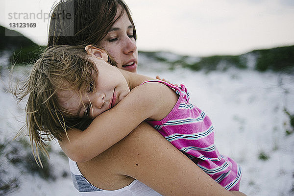 Mutter trägt Tochter  die am Strand schläft