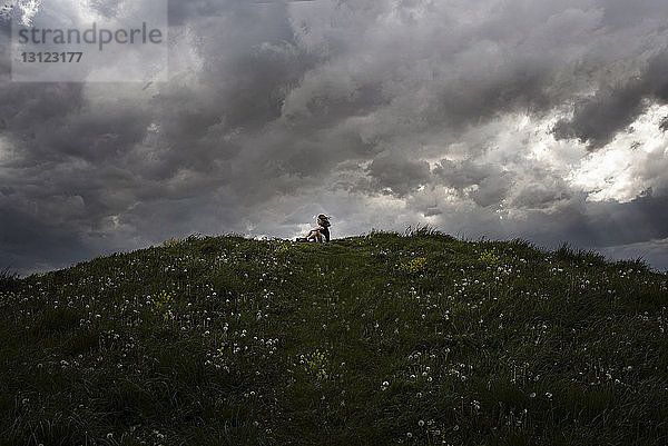 Tiefblick auf ein Mädchen  das auf einem Hügel vor stürmischen Wolken sitzt