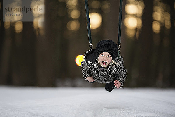 Porträt eines fröhlichen Mädchens  das im verschneiten Park auf der Schaukel spielt