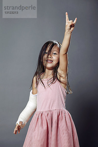 Porträt eines Mädchens mit gestikulierendem Handzeichen vor grauem Hintergrund