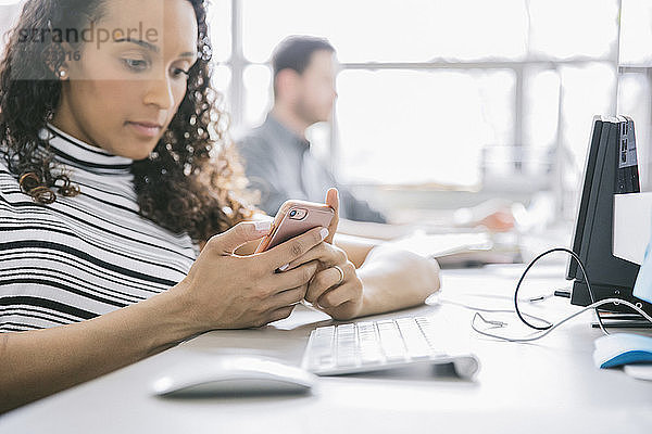 Geschäftsfrau benutzt Mobiltelefon während männlicher Kollege im Hintergrund