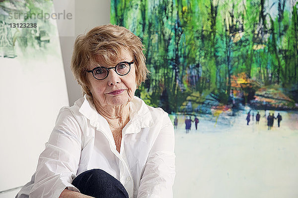 Porträt einer älteren Frau  die zu Hause gegen Gemälde sitzt