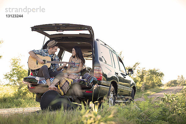 Mann spielt Gitarre für Freundin  während er im Auto sitzt