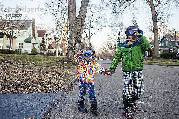 Geschwister  die beim Spielen auf der Straße beim Blick durch das Fernglas Händchen halten