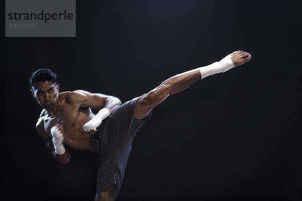 Bestimmter männlicher Kickboxer  der vor schwarzem Hintergrund kickt