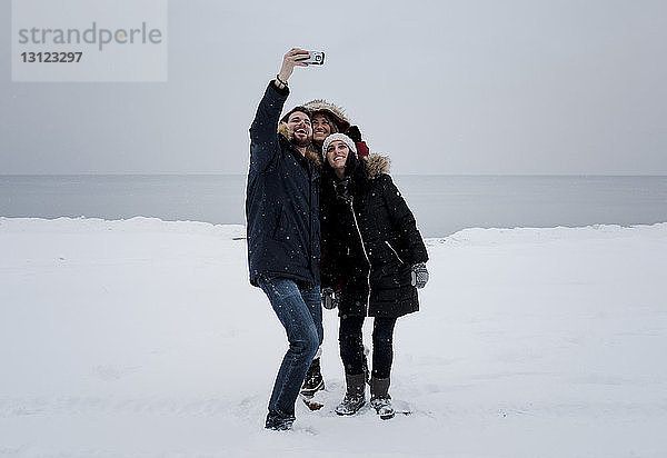 Freunde  die am schneebedeckten Strand gegen den Himmel stehen