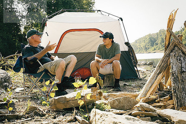 Männliche Freunde unterhalten sich  während sie auf einem Campingplatz am See sitzen