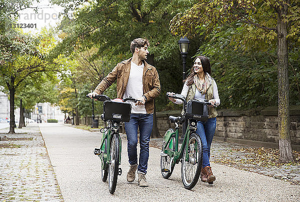 Paar redet beim Gehen mit dem Fahrrad auf der Straße im Park