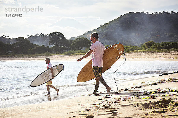 Seitenansicht von männlichen Surfern  die beim Strandspaziergang Surfbretter tragen