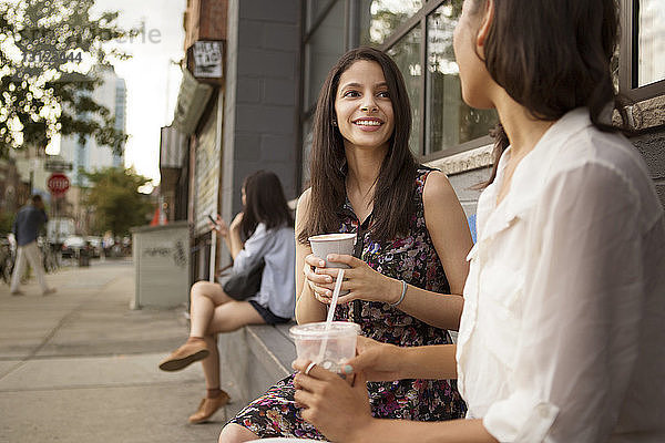 Lächelnde Freunde trinken Kaffee  während sie vor einem Café sitzen