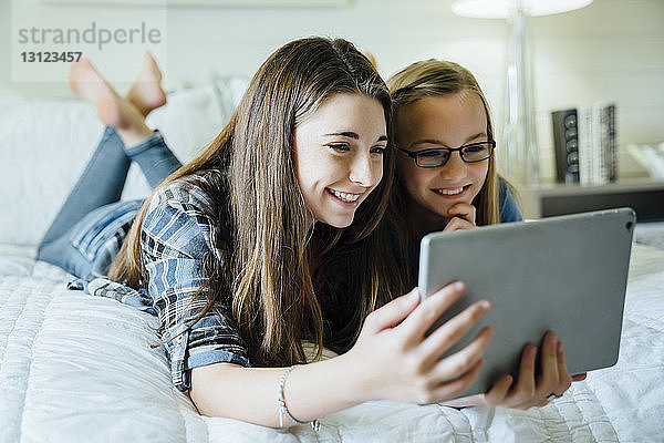 Glückliche Schwestern mit Tablet-Computer im Schlafzimmer