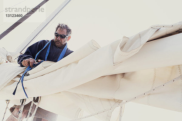 Niedrigwinkelansicht eines Mannes  der die Segel eines Bootes gegen den klaren Himmel bindet