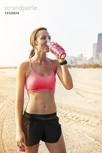 Weibliche Sportlerin trinkt Wasser  während sie am Strand steht