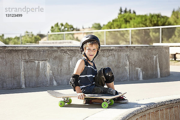 Porträt eines glücklichen Jungen  der im Skateboard-Park sitzt