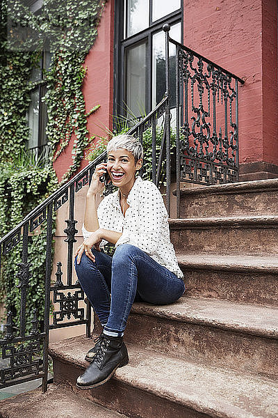 Porträt einer glücklichen Frau  die auf einer Treppe sitzend mit ihrem Handy telefoniert