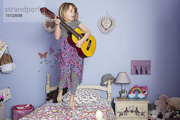 Mädchen hält Gitarre und springt auf dem Bett