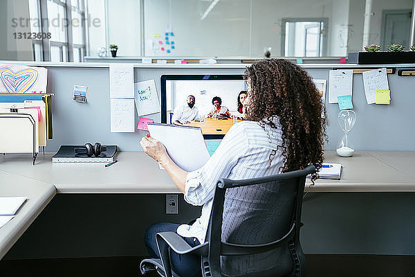 Geschäftsfrau analysiert Dokument bei Videokonferenz mit Kollegen im Büro