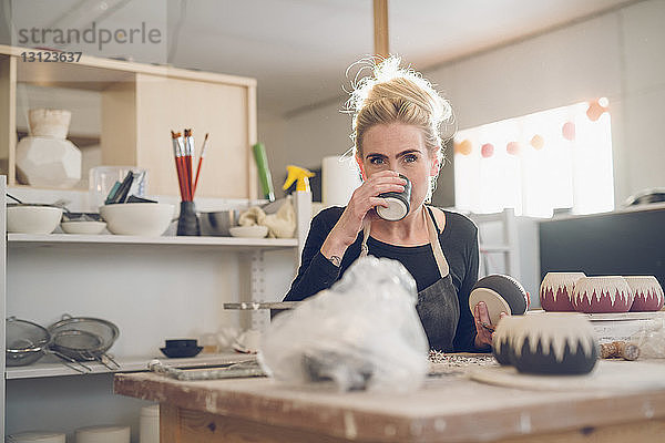 Porträt einer Frau  die in einem Workshop am Tisch sitzt und etwas trinkt