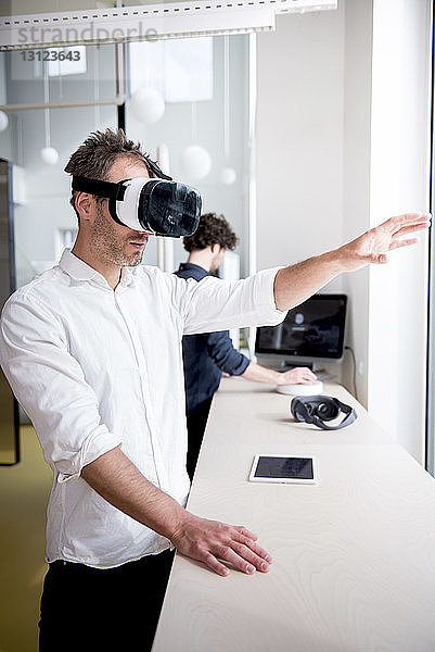 Geschäftsmann untersucht einen Virtual-Reality-Simulator  während ein Kollege den Computer im Büro benutzt