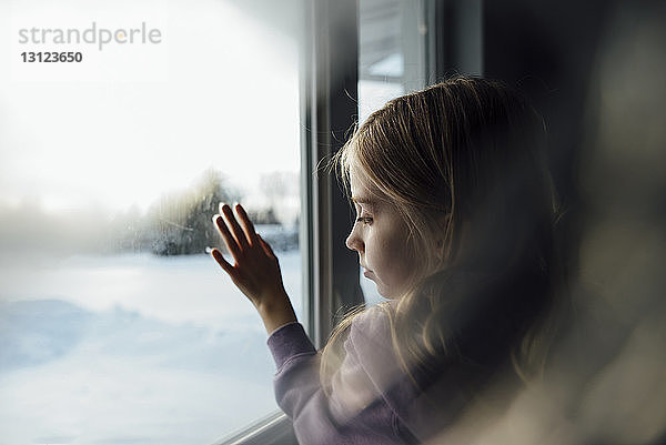 Nachdenkliches Mädchen steht zu Hause am Fenster