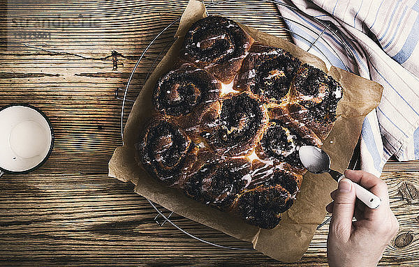 Abgehackte Hand einer Frau  die zu Hause auf einem Holztisch Mohnbrötchen macht