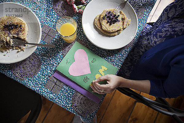 Draufsicht einer Frau  die an ihrem Geburtstag Pfannkuchen nach Glückwunschkarten auf dem Tisch isst