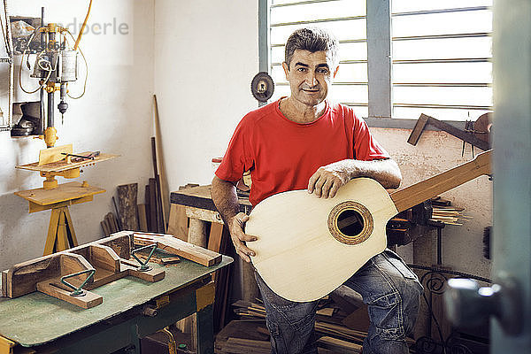 Porträt eines Mannes mit Gitarre in der Hand  während er in der Werkstatt steht