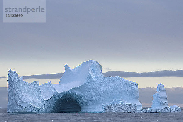 Eisberg im Meer gegen bewölkten Himmel bei Sonnenuntergang