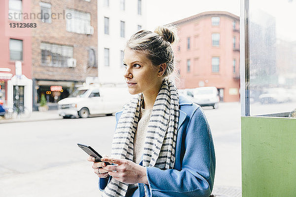 Junge Frau schaut weg  während sie in der Stadt ein Smartphone benutzt