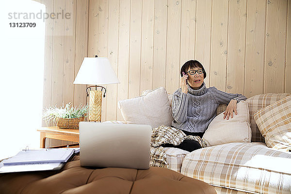 Ältere Frau benutzt Smartphone  während sie zu Hause auf dem Sofa sitzt