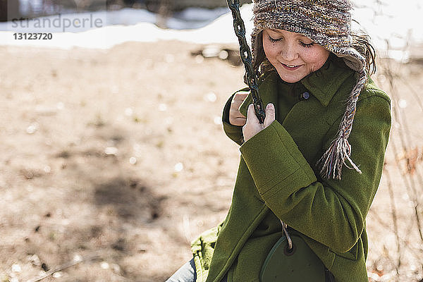 Lächelndes Mädchen schaukelt im Winter auf dem Spielplatz