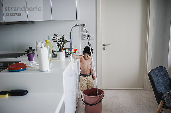 Junge ohne Hemd füllt zu Hause Wasser in Eimer