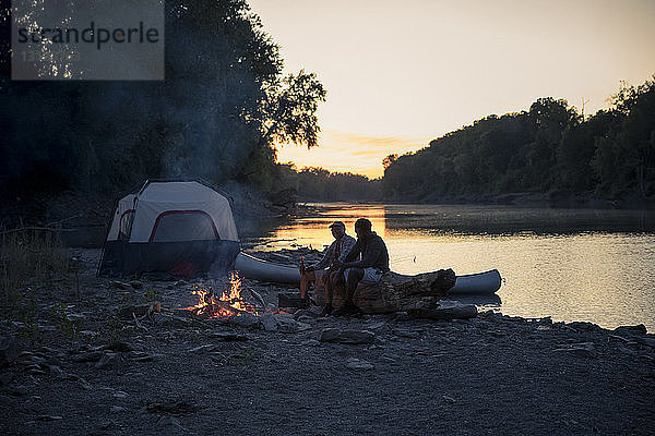 Männliche Freunde entspannen sich bei Sonnenuntergang auf einem Campingplatz am See gegen den Himmel