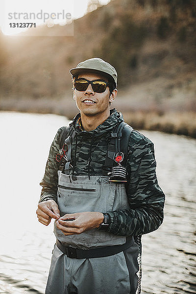 Porträt eines männlichen Wanderers mit Sonnenbrille  der im Fluss gegen den Berg steht