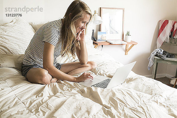 Lächelnde Frau benutzt Laptop-Computer  während sie auf dem Bett sitzt