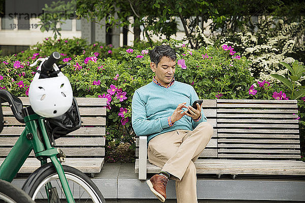 Ein erwachsener Mann benutzt ein Smartphone  während er im Park auf einer Bank sitzt