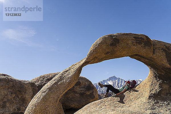 Weibliche Wanderin liegt auf Felsformation vor blauem Himmel