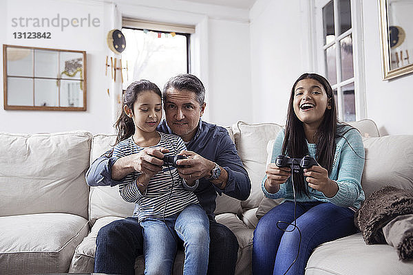 Mädchen mit Vater spielen Videospiel  während sie zu Hause auf dem Sofa sitzen