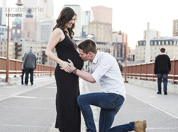 Ehemann küsst den Bauch seiner schwangeren Frau  während er auf der Straße in der Stadt steht