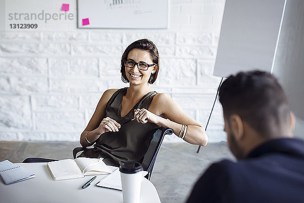 Lächelnde Geschäftsfrau sitzt auf Stuhl im Kreativbüro