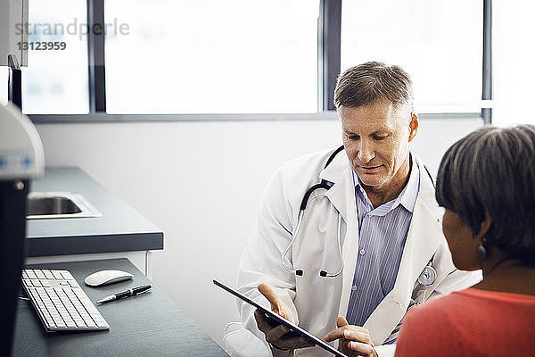 Männlicher Arzt zeigt dem Patienten in der Klinik Bericht auf Tablet-Computer