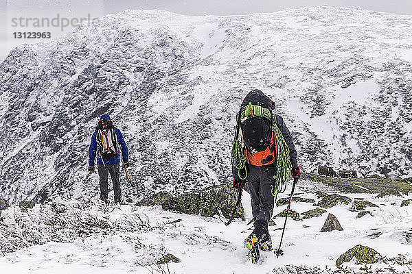 Rückansicht von Rucksacktouristen  die im Winter auf einem schneebedeckten Berg stehen