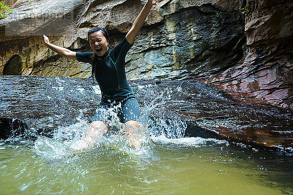 Fröhliche Frau springt in Teich von Felsformation