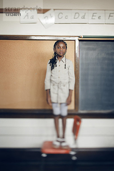 Porträt eines auf einem Stuhl stehenden Mädchens vor einer Tafel im Klassenzimmer